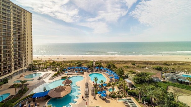 A hotel with multiple swimming pools, a beach view, and a large building in the background.
