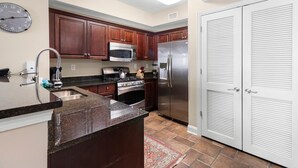 A kitchen with dark wooden cabinets, stainless steel appliances, a granite countertop, and a tiled floor. - Penthouse Elegance by the Sea 3BR Condo with Views (North Myrtle Beach)