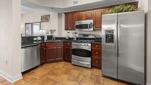 A modern kitchen with stainless steel appliances, wooden cabinets, and a tiled floor.