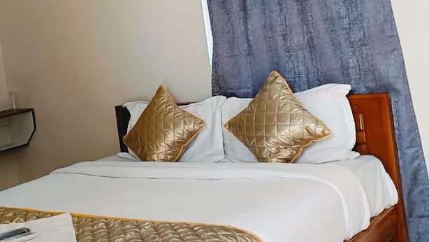 A neatly made bed with a white and gold bedspread, two gold pillows, and a wooden headboard. - Eben Residency (Chengalpattu)