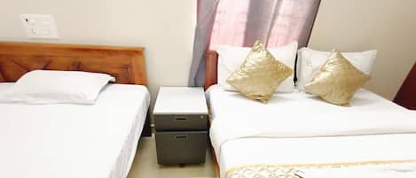 A hotel room with two single beds, a small bedside table, a nightstand, and a suitcase on the floor.