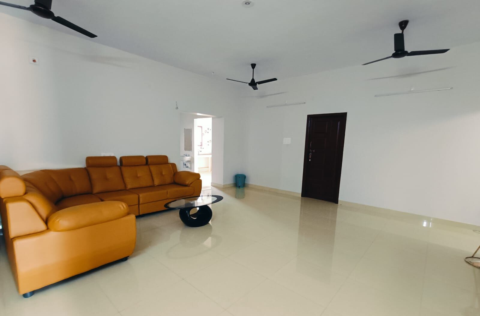 A spacious living room with a large orange sofa, a coffee table, and two ceiling fans.