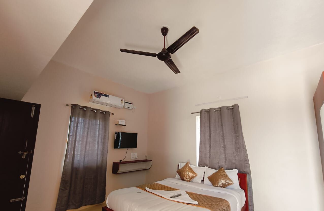 Un dormitorio con cama, ventilador de techo, aire acondicionado, televisor y cortinas.