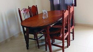 A dining table with four wooden chairs, a clear glass pitcher, and a dark curtain partially drawn. - Eben Residency (Chengalpattu)