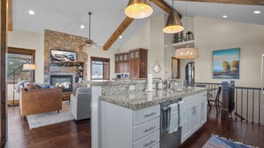 A spacious living area with a fireplace, a stone accent wall, and a large island with a sink.