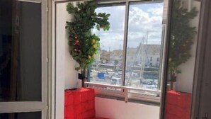 A small balcony with a red cushioned bench, a potted plant, and a view of a marina. - sun and boat (Courseulles-sur-Mer)
