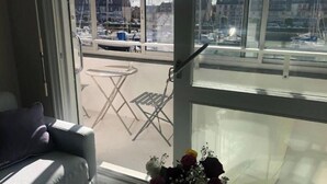 A room with a view of a marina through large windows, a grey sofa, and a small table. - sun and boat (Courseulles-sur-Mer)