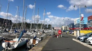 A marina with multiple sailboats docked, a pathway, and buildings in the background. - sun and boat (Courseulles-sur-Mer)