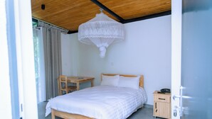 A bedroom with a wooden bed, a small wooden nightstand, a desk, and a hanging white chandelier. - Don Bosco Hospitality Centre (Kigali)