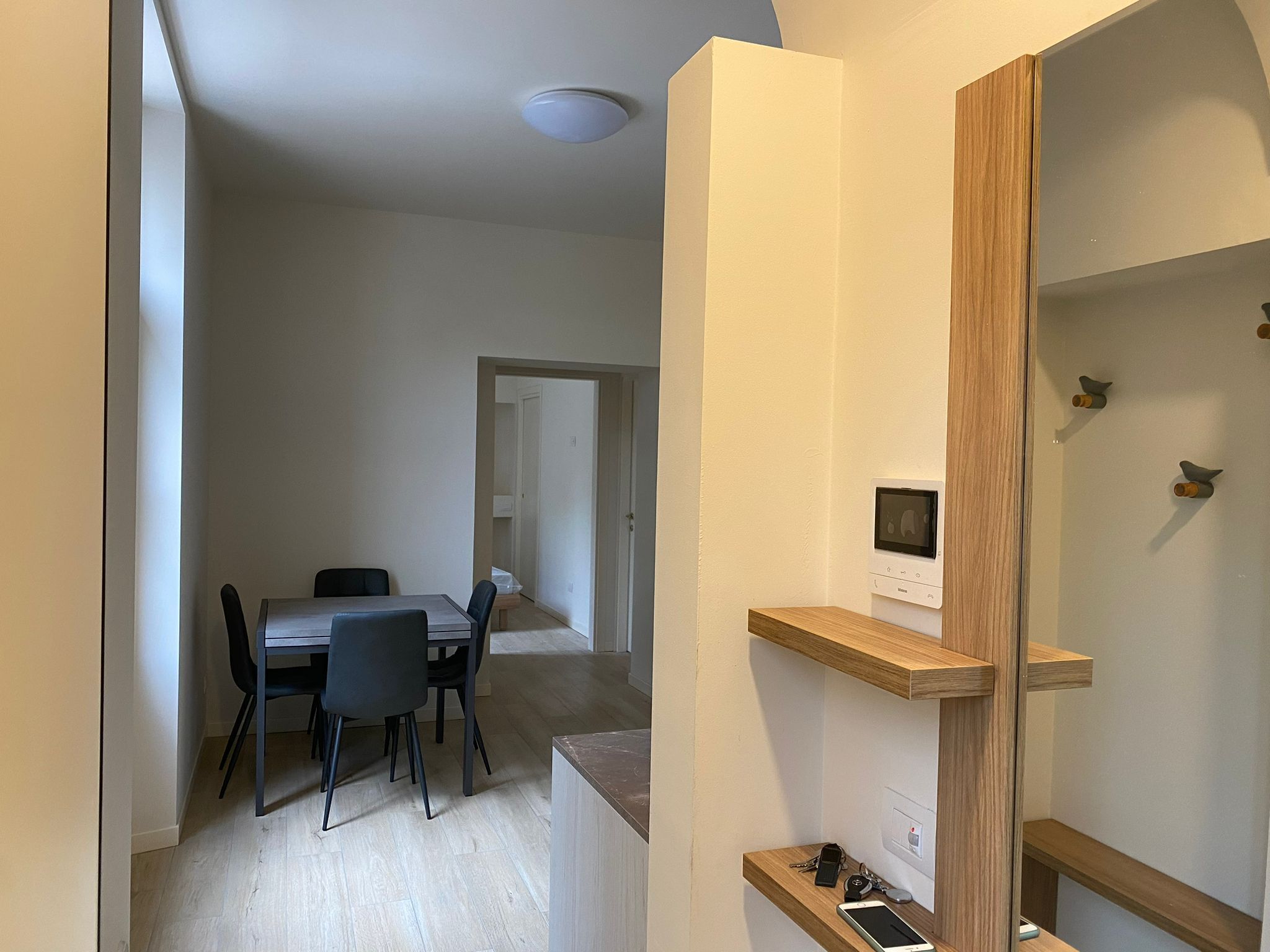 A modern interior with a dining area, a built-in shelf with keys and a phone, and a ceiling light.