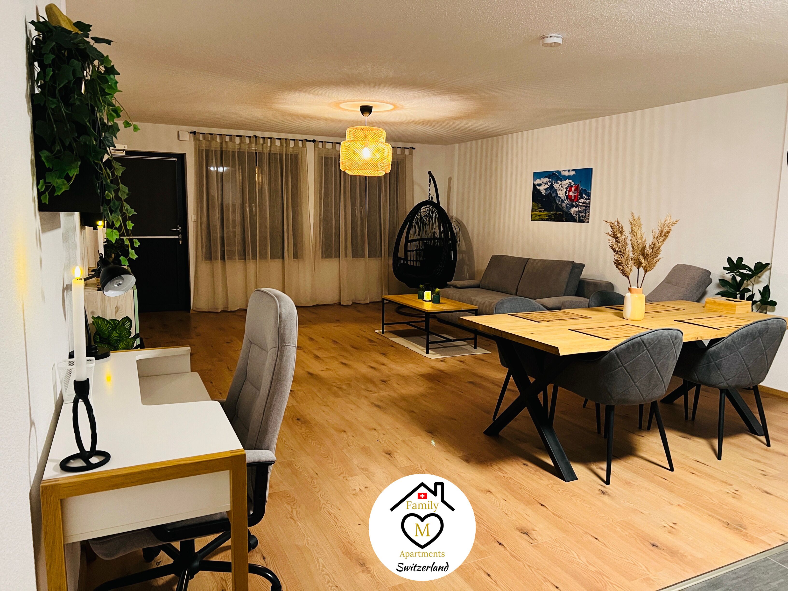 Ein modernes Wohnzimmer mit Essbereich, Holzboden, grauen Sofas und einem Hängesessel.