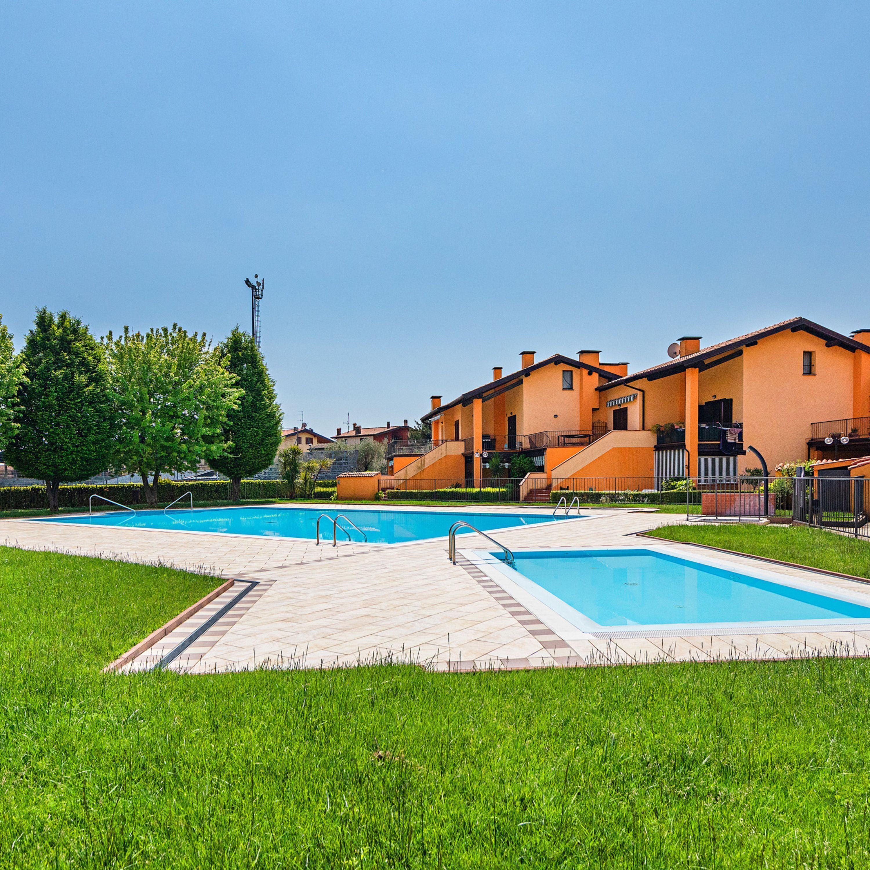 A residential area with a swimming pool, houses with orange walls, and a clear sky.