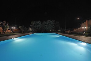 Ein Schwimmbad bei Nacht mit umgebenden Gebäuden und Straßenbeleuchtung.