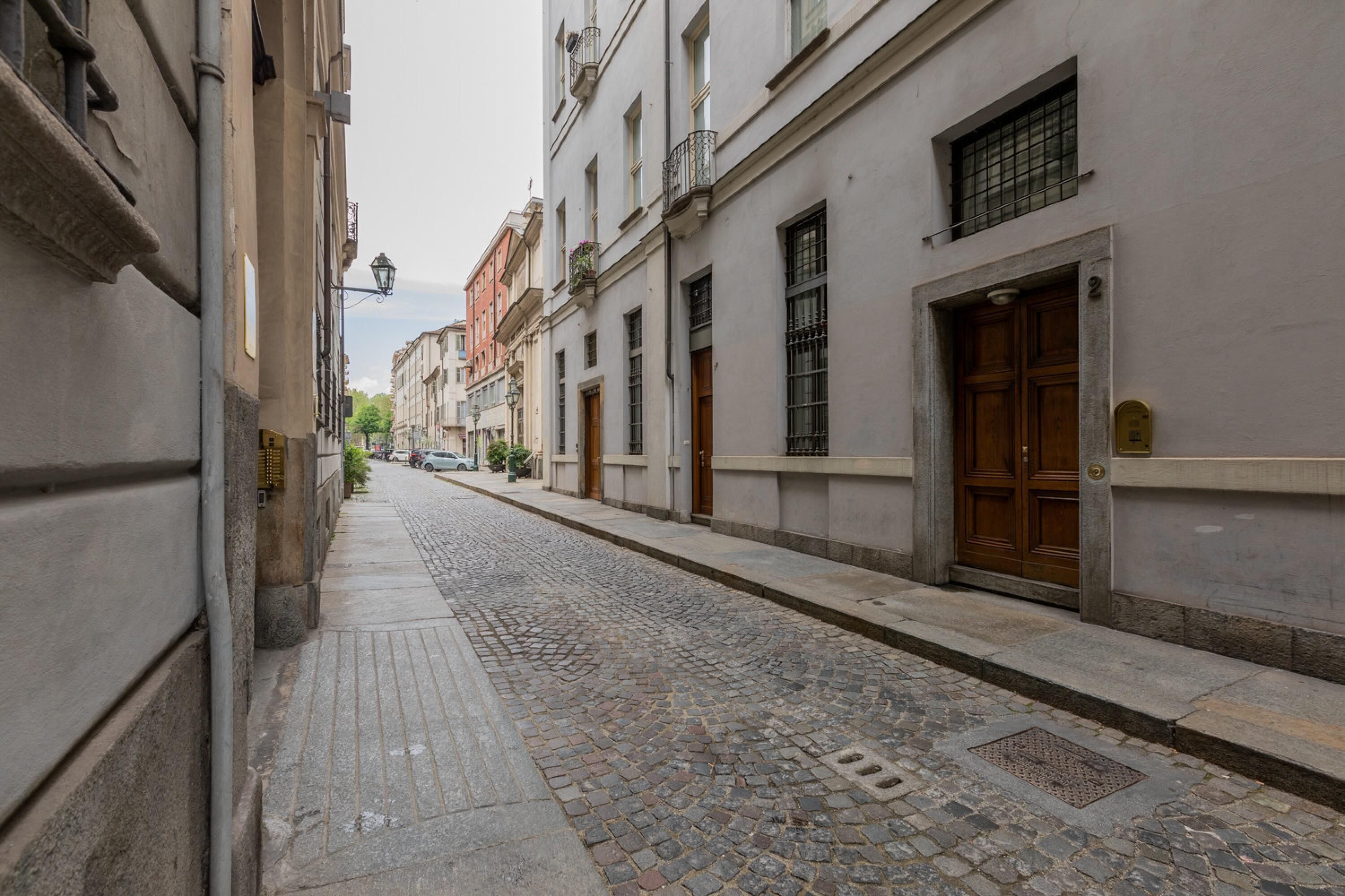 A cobblestone street lined with historic buildings, featuring a variety of architectural styles and a narrow sidewalk.