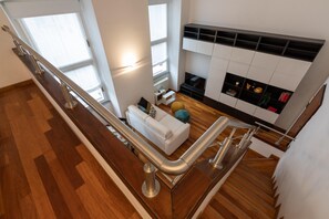 A modern living room with a white sofa, a glass railing, a fireplace, and a wooden floor.