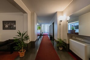 A hotel hallway with a red carpet, potted plants, a black sofa, and a wall-mounted mirror. - Il Colibr by Wonderful Italy (Turin)