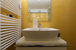 A bathroom with a white sink, yellow tiles, a mirror, and a small potted plant. - Il Colibr by Wonderful Italy (Turin)
