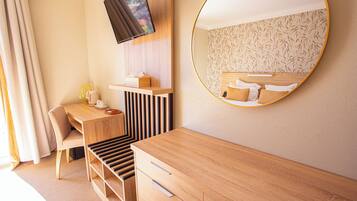 Een moderne hotelkamer met een houten bureau, een stoel, een aan de muur bevestigde televisie en een grote spiegel die het bed weerspiegelt.
