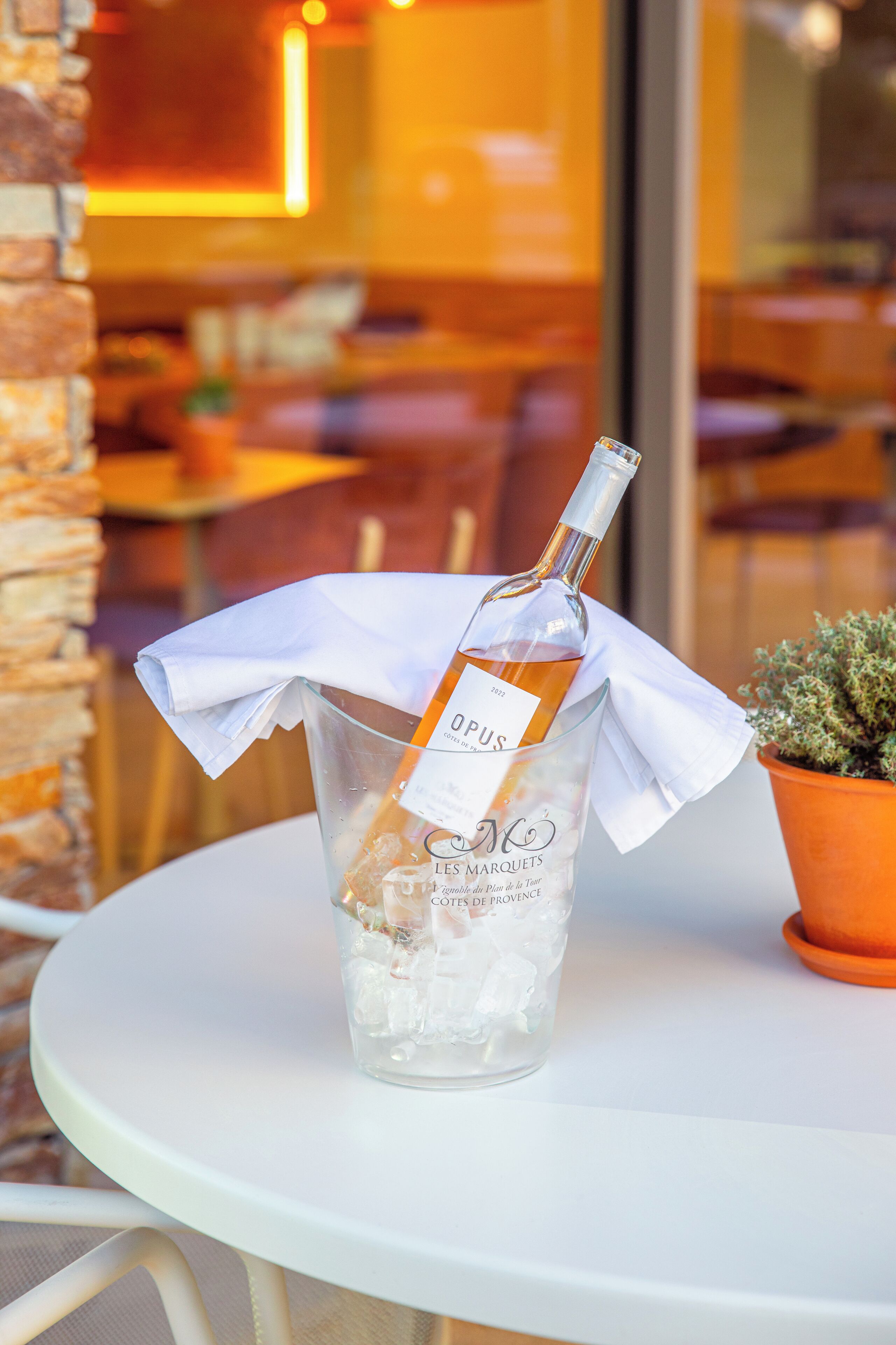 A bottle of wine in a glass with ice, placed on a white table outdoors.