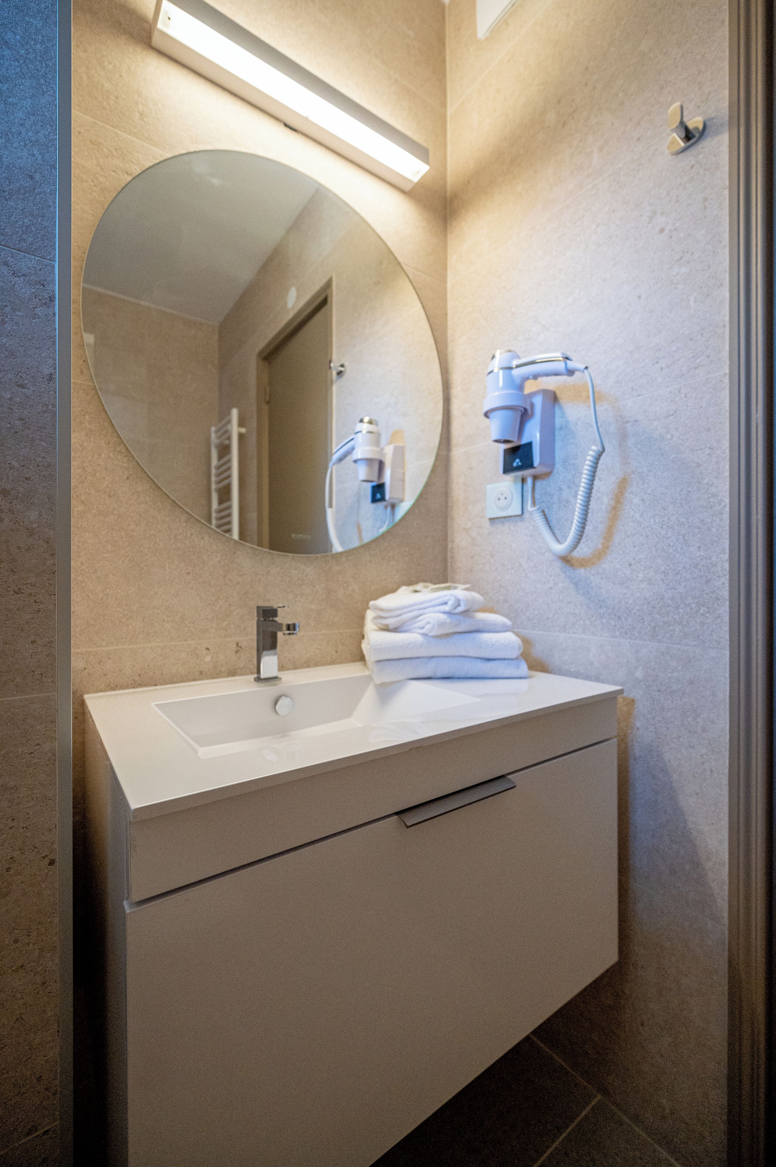 A modern bathroom with a white sink, a round mirror, and a towel rack.