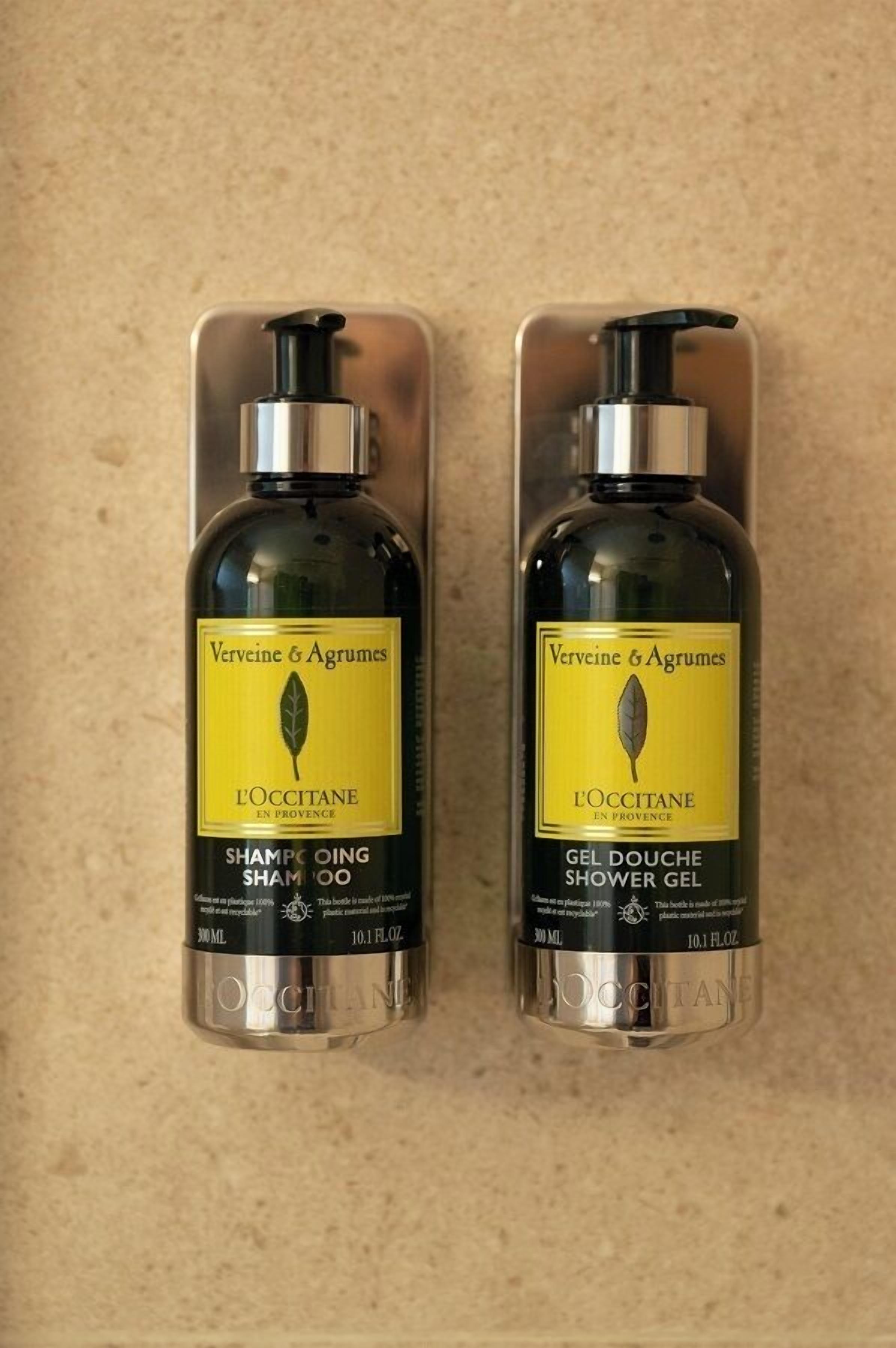 Twee flessen Verveine & Agrumes L'OCCITANE shampoo en douchegel op een beige aanrecht.