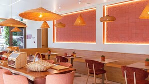 Un caffè moderno con tavoli in legno, sedie rosse e lampade intrecciate color arancione.