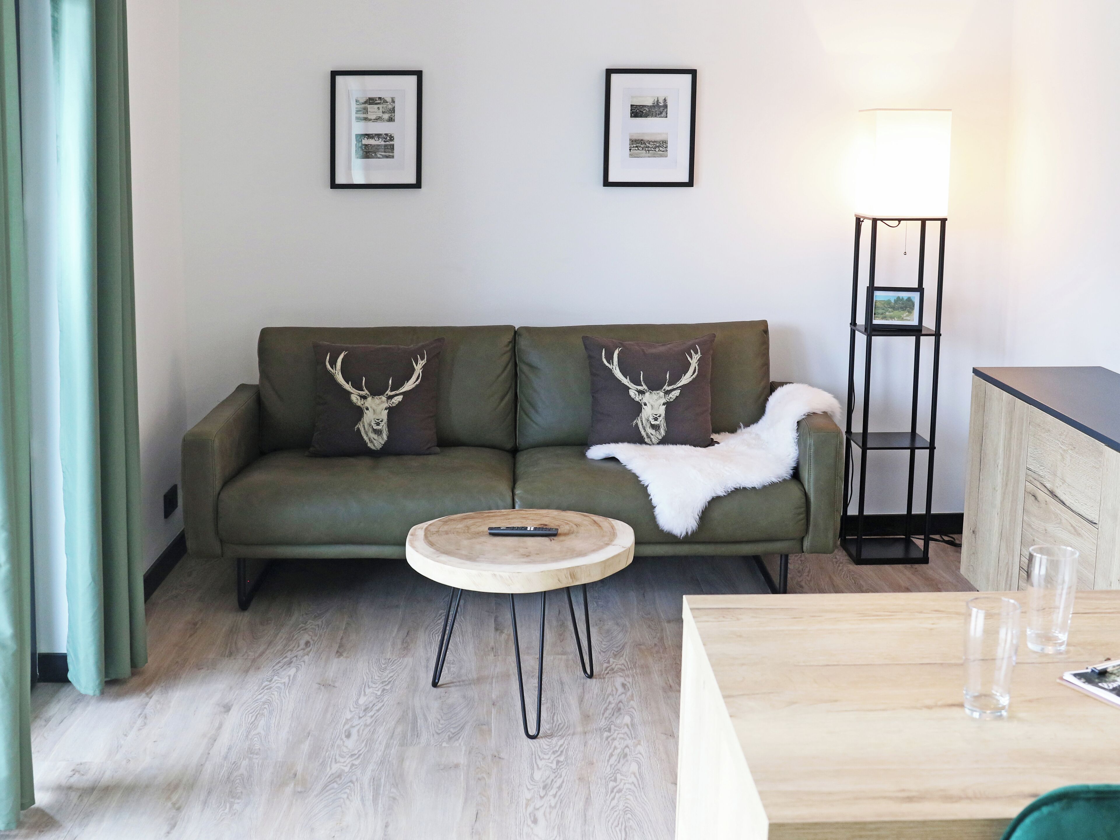 Una sala de estar con un sofá verde, dos almohadones con motivos de ciervo, una mesa de centro redonda de madera y una lámpara de pie.