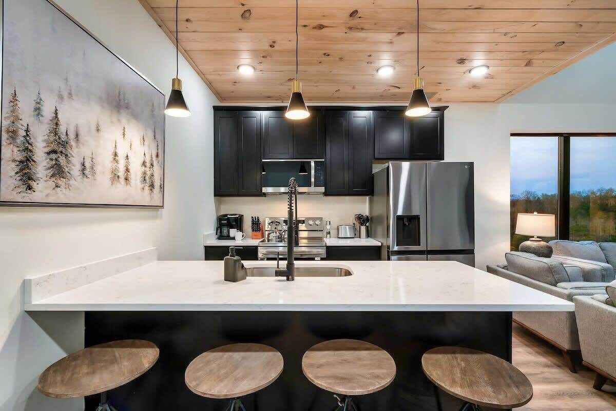 Une cuisine moderne avec des meubles de couleur sombre, des appareils en acier inoxydable et un grand îlot central doté de tabourets.