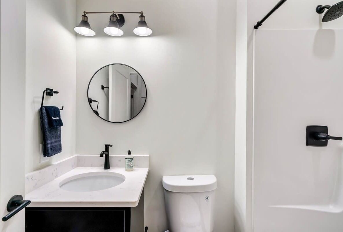 Une salle de bain moderne avec un lavabo blanc, un miroir rond et des toilettes. On y trouve un porte-serviettes sur lequel est accrochée une serviette.