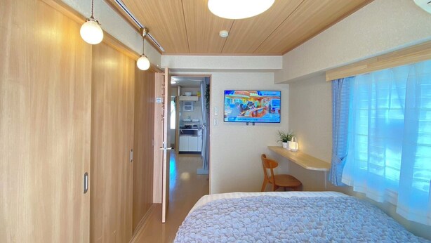 A bedroom with a bed, wooden wardrobe, a television on the wall, and a window with curtains. - G301#[new Open]jr5 (Shinjuku-ku)