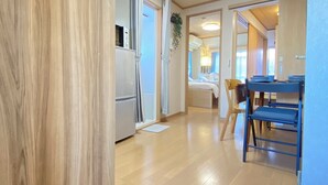 A modern kitchen with a refrigerator, a dining area with blue chairs, and a visible bed in the background.