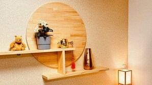 A wooden shelf with a teddy bear, a potted plant, a golden vase, and a hanging ornament.