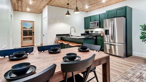 A modern kitchen with green cabinets, stainless steel appliances, and a wooden dining table set with black bowls.