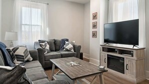 Un salon moderne avec un canapé gris, une table basse, un téléviseur à écran plat et une cheminée.