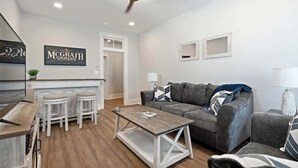 Un salon moderne avec un canapé gris, une table basse et un coin bar équipé de tabourets.