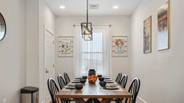 Un espace repas avec une longue table en bois, des chaises noires et un luminaire suspendu.