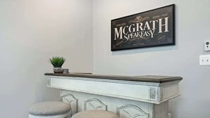 Un coin bar avec une enseigne indiquant « McGrath SpeakEasy » et deux tabourets.
