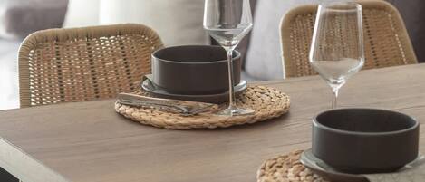 A dining table with two dark bowls, two wine glasses, and a cake on woven placemats.