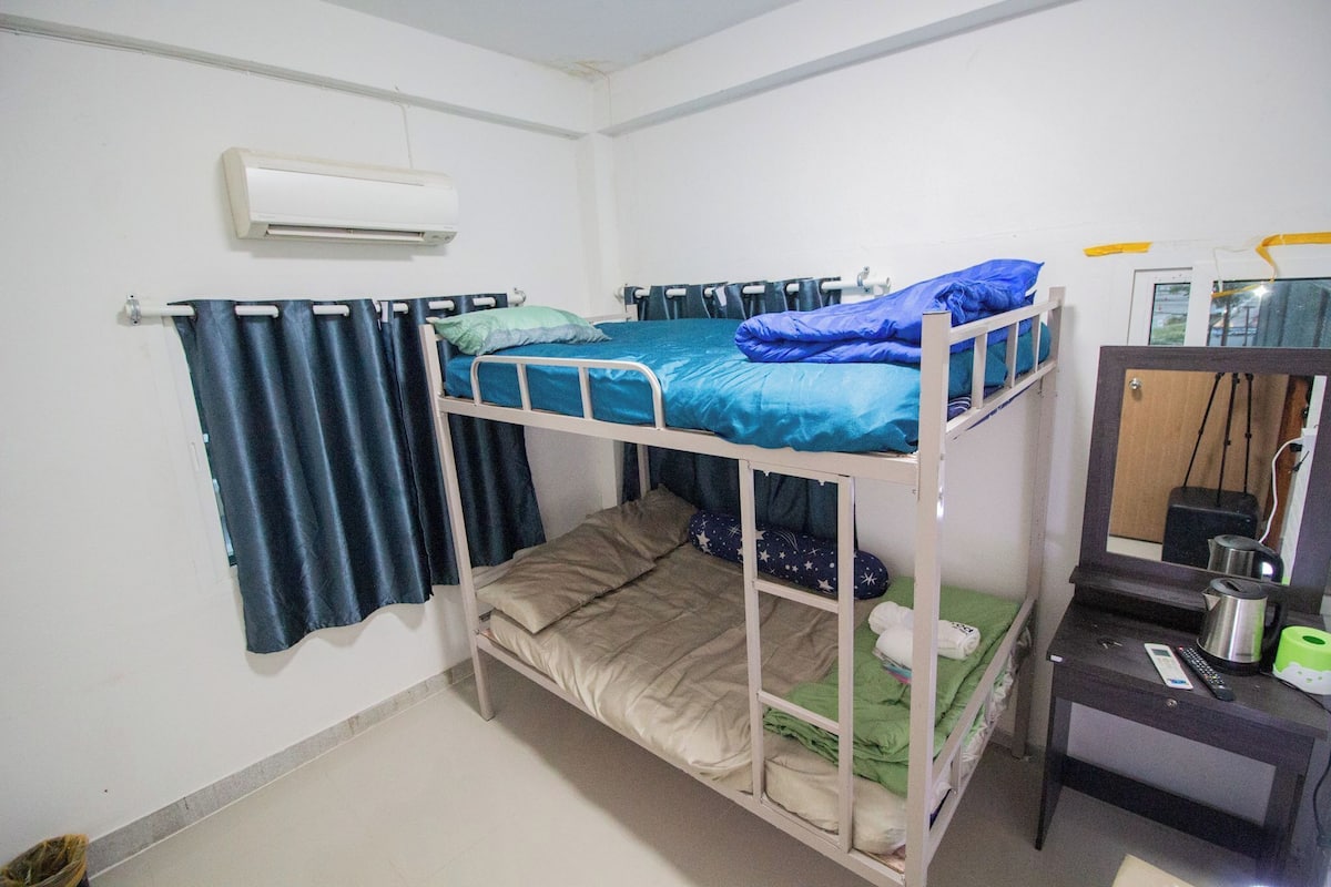 A bunk bed room with a mirror, a small table with a kettle, and a curtain.