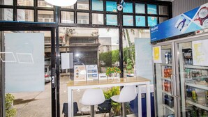 Ein Hotel-Empfangsbereich mit Glastür, Empfangstresen, zwei weißen Stühlen, einem mit Getränken gefüllten Kühlschrank und einem Schild, das Frühstück und Autoverleih anbietet.