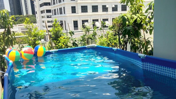 Ein Swimmingpool mit blauen Fliesen und aufblasbaren Bällen, umgeben von Grünflächen und Gebäuden.