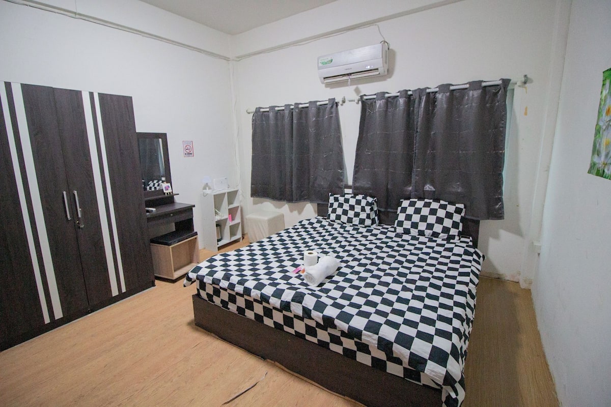 A bedroom with a checkered bedspread, a wardrobe, a desk, and a shower curtain.