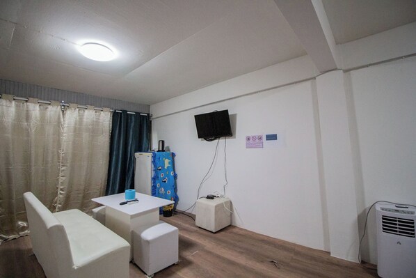 A small, private room with a white desk, a chair, a television mounted on the wall, and a heater.