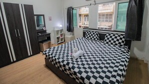 Ein Schlafzimmer mit karierter Bettdecke, einem Kleiderschrank, einem Schreibtisch mit Lampe und einem Fenster mit Vorhängen.