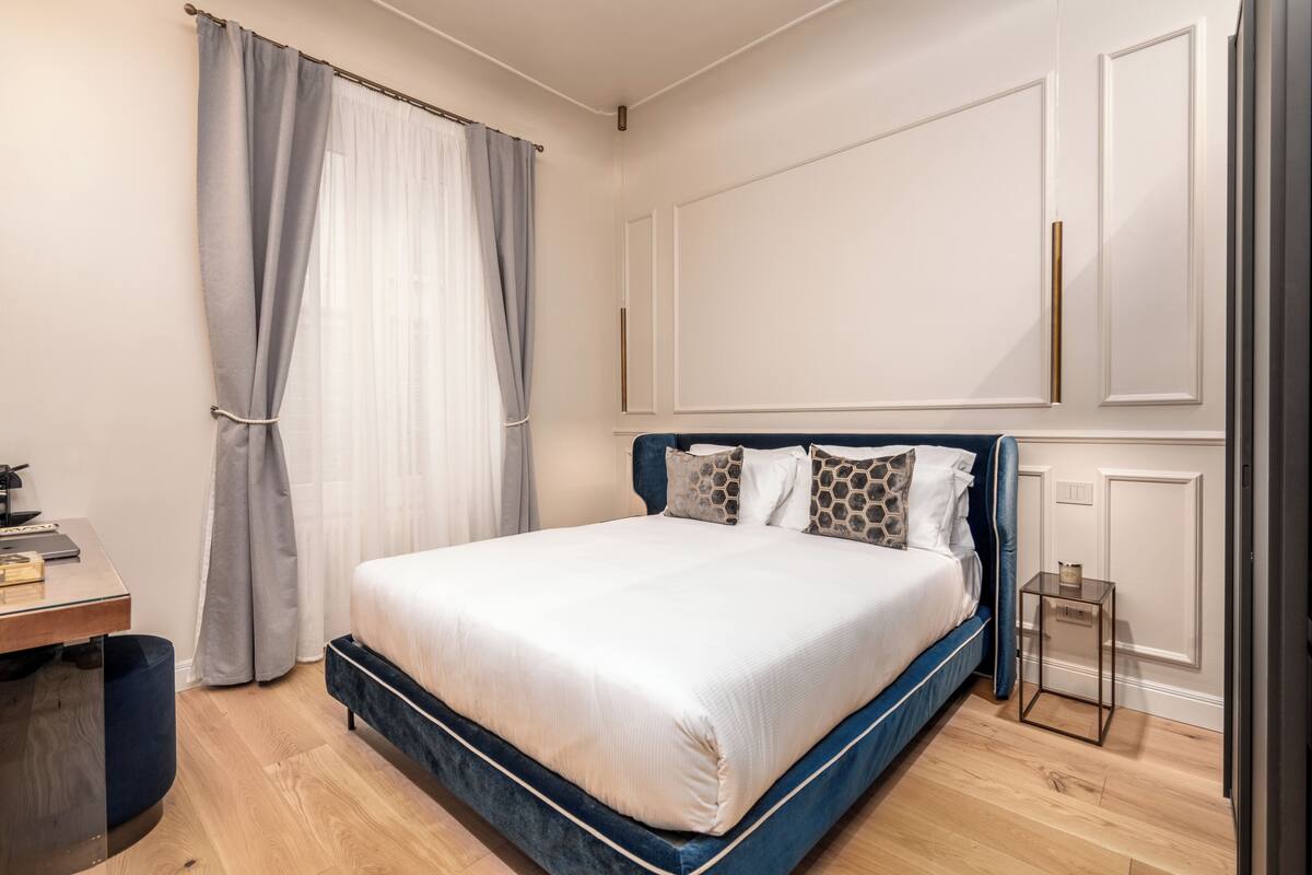 A bedroom with a bed, curtains, a desk, and a small table.