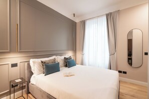 Un lit bien fait, avec des oreillers, une table de chevet sur laquelle repose un livre et un grand miroir accroché au mur.