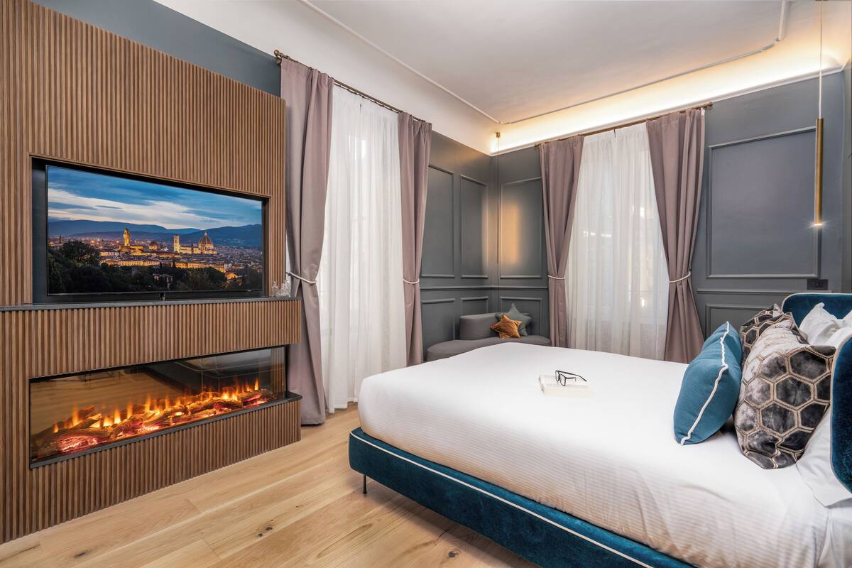 A modern bedroom with a large bed, a flat-screen TV mounted on a wooden panel, and a fireplace.