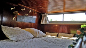 A bedroom with a wooden ceiling, a bed with patterned bedding, a sign on the wall, and a window with curtains.