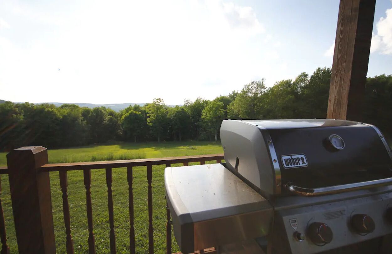 Una parrilla para barbacoa en una terraza de madera con vista a un campo cubierto de césped y árboles.