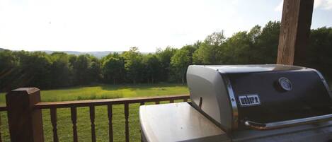 Una parrilla para barbacoa en una terraza de madera con vista a un campo cubierto de césped y árboles.